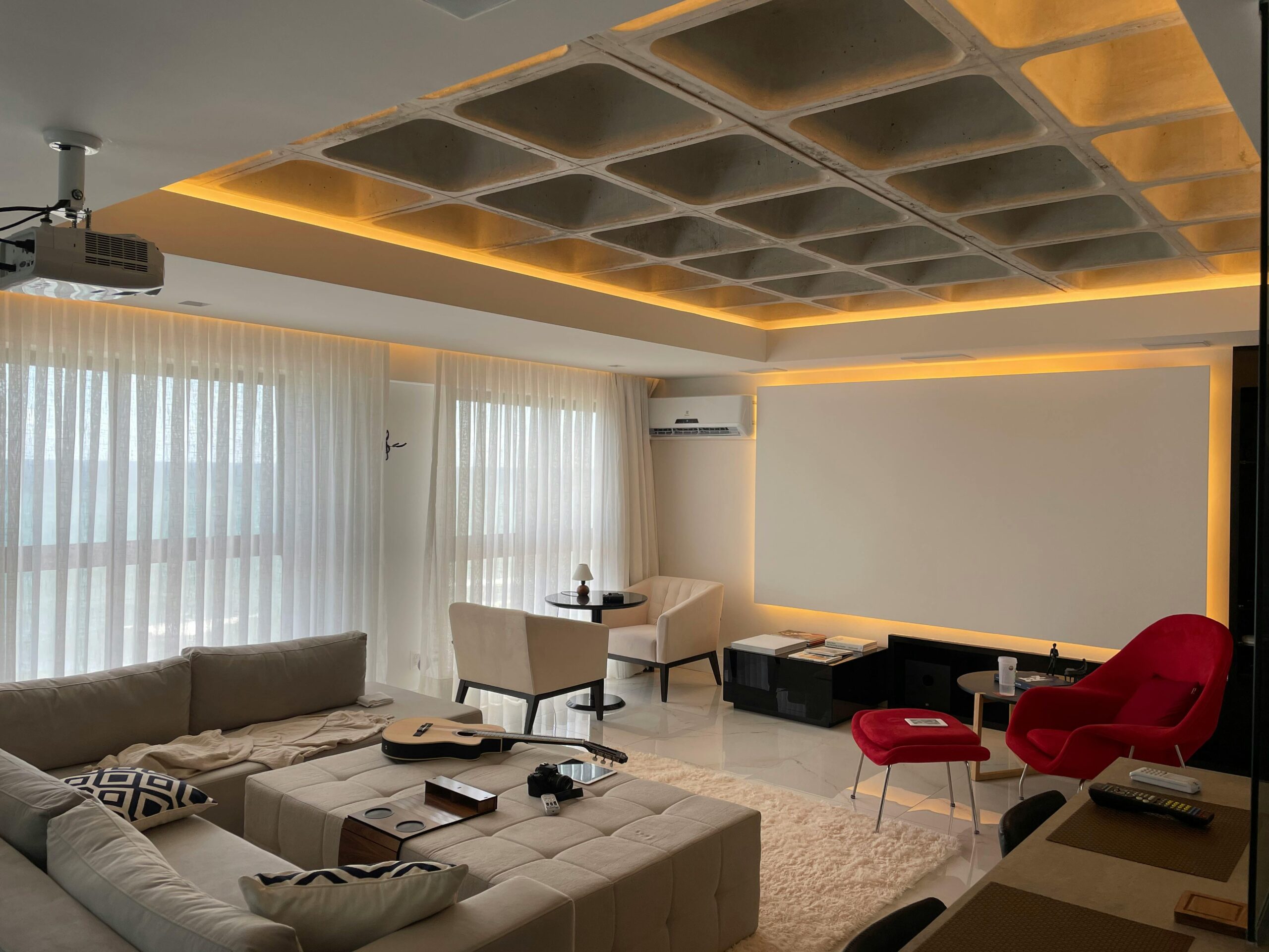 Interior of modern light bedroom with pillows and blanket on bed under lamps next to pouf near glass wall with curtain